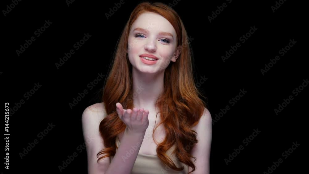 Wall mural Attractive young woman with red long hair sending air kiss isolated over black 