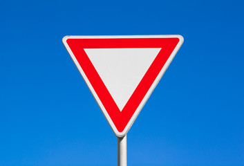 Give way / Yield - red and white triangle. Clear blue sky is behind road sign.
