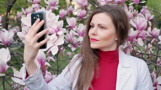 beautiful girl among magnolia pink blossom sping tree flowers making selfie