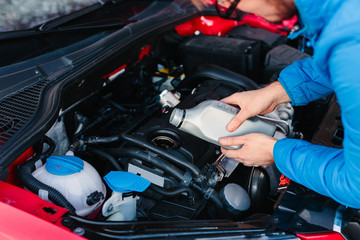 Male adding oil under the hood of the car. DIY oil change.