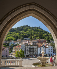 Portugal , Sintra . View of the city through the lancet arch main entrance to the royal palace . Fountain, paved stone wild area of the palace . - obrazy, fototapety, plakaty