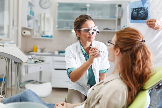 A professional female dentist, equipped with a bright smile, converses with her red hair female patient, carefully explaining the upcoming treatment, and ensuring her comfort throughout the process.