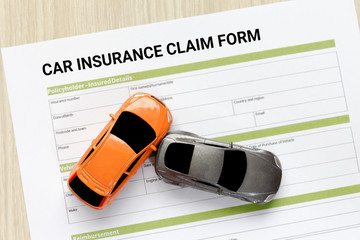 Top view of car insurance claim form with car toy crash on wooden desk.