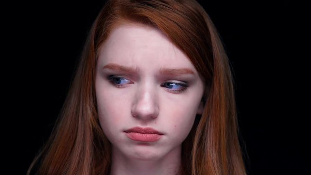 Close-up of unhappy dissatisfied young red haired woman looking at camera isolated over black 