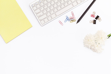yellow legal pad, keyboard, paper clips, a pencil and a chrysanthemum flower on a white background. Flat lay concept of the workplace in the office.