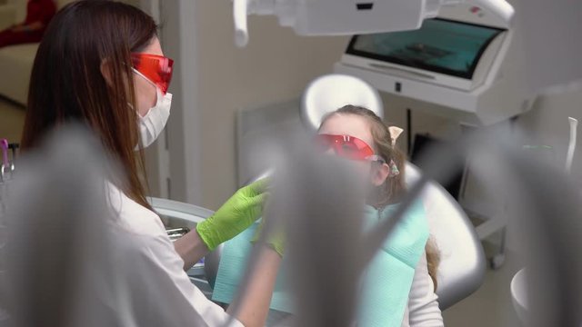 Little cute girl at dentist clinic gets dental treatment to fill a cavity in a tooth. Dental restoration and material polymerization with UV light. Shot in 4k