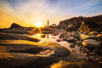 An ancient lighthouse at dawn, a reflection of a lighthouse in the water among the stones. A ...