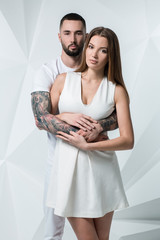 Young casual couple with woman holding his hands over woman's shoulder and looking for the camera. On white background