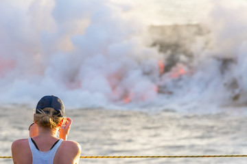 Tourist photographing the lava pouring into the sea in Volcanoes National Park, Big Island, Hawaii