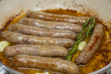 Homemade lamb sausage with rosemary and garlic is fried in a frying pan in olive oil