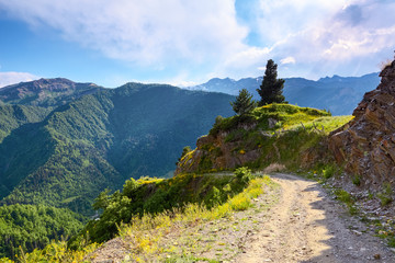 A wide road with a cliff leads down to the high Caucasus mountains.