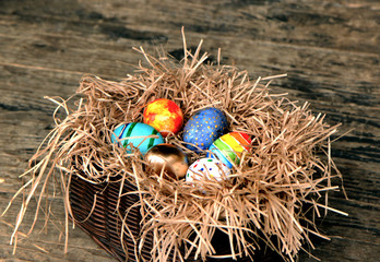 Easter colorful eggs in the nest on wooden background.