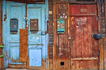 Old shabby wooden doors with peeling paint and mailboxes. Russia.