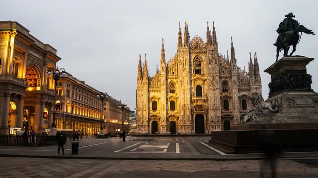 Milan, Italy. Cathedral of Milan, Italy at sunrise - famous landmark in the city. Motion blurred people, illuminated Gallery entrance, cloudy sky in the morning. Time-lapse