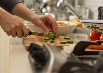 Woman cutting cucumber on wooden chopping board to prepare green salad