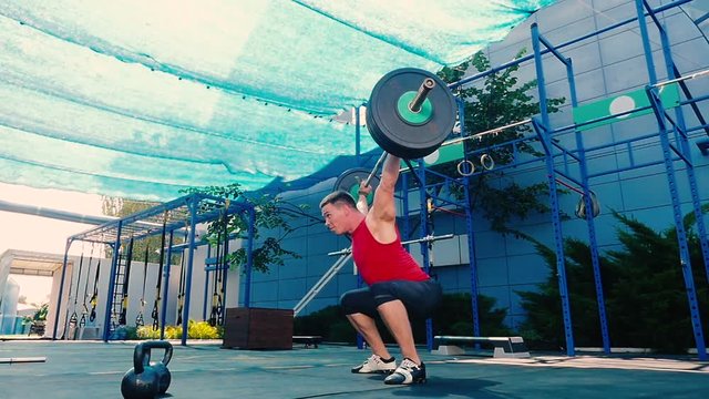 Strong man training with barbell on the sports ground