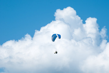 Paragliding in the blue sunny sky. One paraglider fly in summer sunny day in the clouds. Carpathians, Ukraine. Paragliding over the mountain valley.
