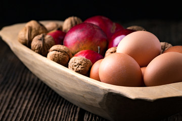 Wooden bowl with apple, eggs and walnut