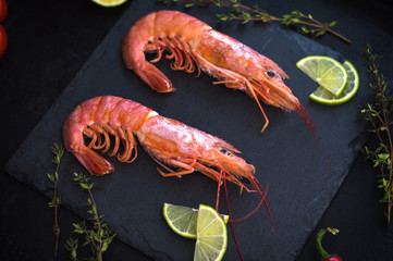 Shrimp on a stone with cherry tomatoes, lime and thyme in a restaurant. Cooking process. Black background. Top view. Close-up