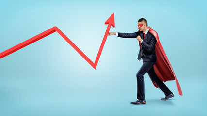 Obraz premium A businessman in a red superhero cape throwing punches at a red statistic arrow pointing upwards.