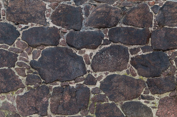 Background of dark stones of red terracotta color fastened by cement wall