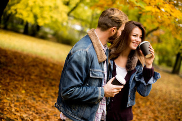 Fototapeta premium Happy young couple with coffee cups walking in autumn park