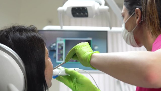 Young female dentist examining the mouth of a patient with an intraoral camera and showing image on the screen. Shot in 4k