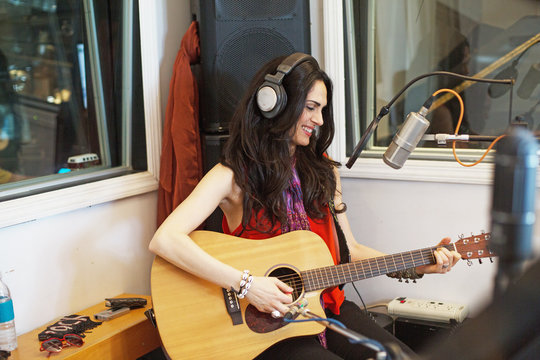 Smiling young woman playing acoustic guitar in recording studio