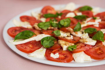 Tomato and mozzarella salad with basil leaves, sprinkled with pepper, olive oil and acceto balsamico on the white plate