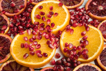 Slices of sicilian orange and common orange with scattered pomegranate seeds. Super macro photo of fruits. Top view at slices of fruits.