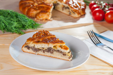 Fresh piece of closed pie with potatoes and mushrooms on the white plate on the wooden served table. Composition of ingridients. Selective Focus, close up
