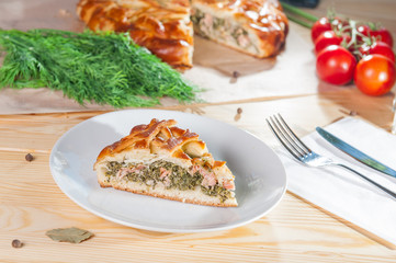 Fresh piece of closed pie with trout and spinach on the white plate on the wooden served table. Composition of vegetables and ingridients. Selective Focus, close up