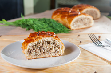 Fresh piece of meat closed pie on the white plate on the wooden served table. Composition of vegetables and ingridients. Selective Focus
