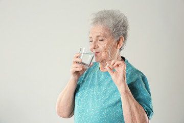 Elderly woman taking pill on light background