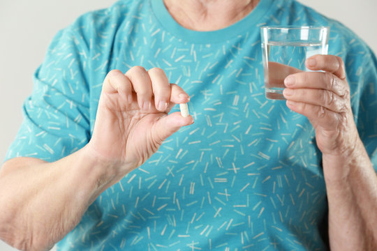 Elderly woman with pill and glass of water on light background, closeup