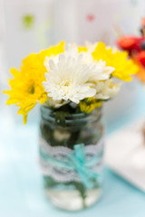 Yellow and white chrysanthemums in a glass decorated jar with blue ribbon and lace. Baby shower, wedding decoration. Flower decoration