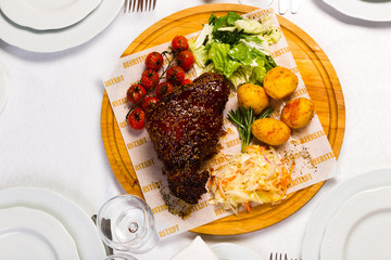 Grilled meat with garnish of vegetables on a wooden round board, studio light