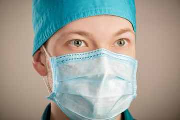 male surgeon in mask looking at camera on grey background, close up