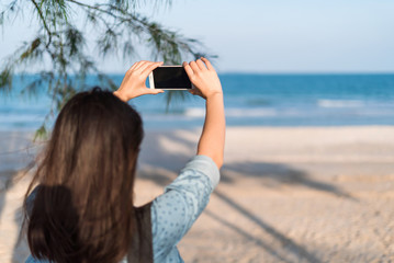 Woman traveler taking photos with smartphone at the beach.