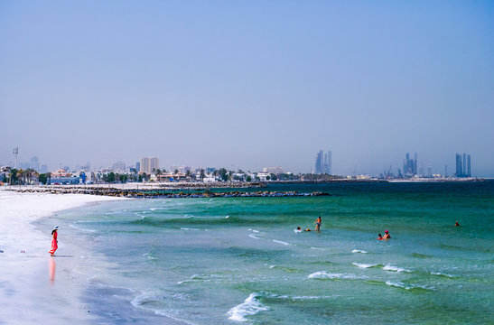 Dubai. Summer 2016. The Persian Gulf with the line of the beach from the Ajman. Woman in red plays on the beach.