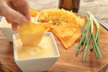 Female hand dipping nacho in bowl with beer cheese dip, closeup