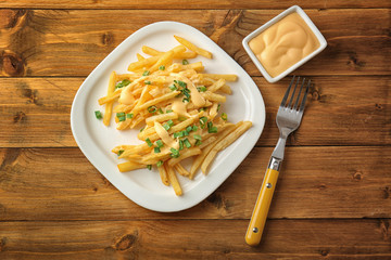 Plate with cheese fries and chopped green onion on wooden table