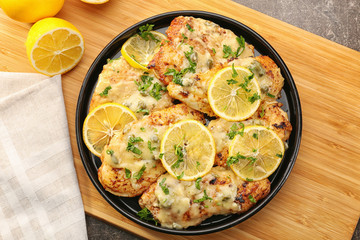 Plate with delicious chicken piccata on wooden board