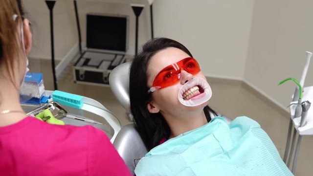 Young woman with an expander in mouth at the dental clinic. Application of whitening gel to the teeth. Modern dental office. Shot in 4k