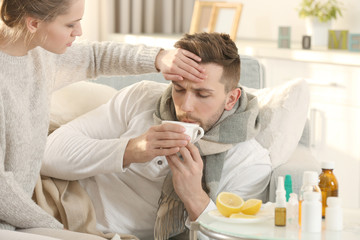 Young woman taking care of ill man lying on sofa at home