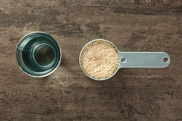 Rice in measure scoop with glass of water on kitchen table
