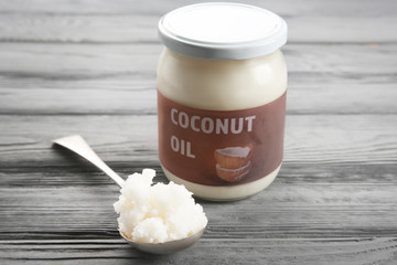 Spoon near glass jar with fresh coconut oil on grey wooden background