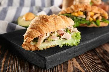 Wooden board with chicken salad in croissant bun on table