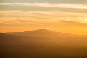Obraz premium A mountain and some hills in the middle of a golden, orange light during sunset, with clouds also reflecting light