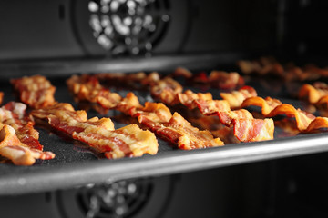 Baking tray with strips of bacon cooking in oven
